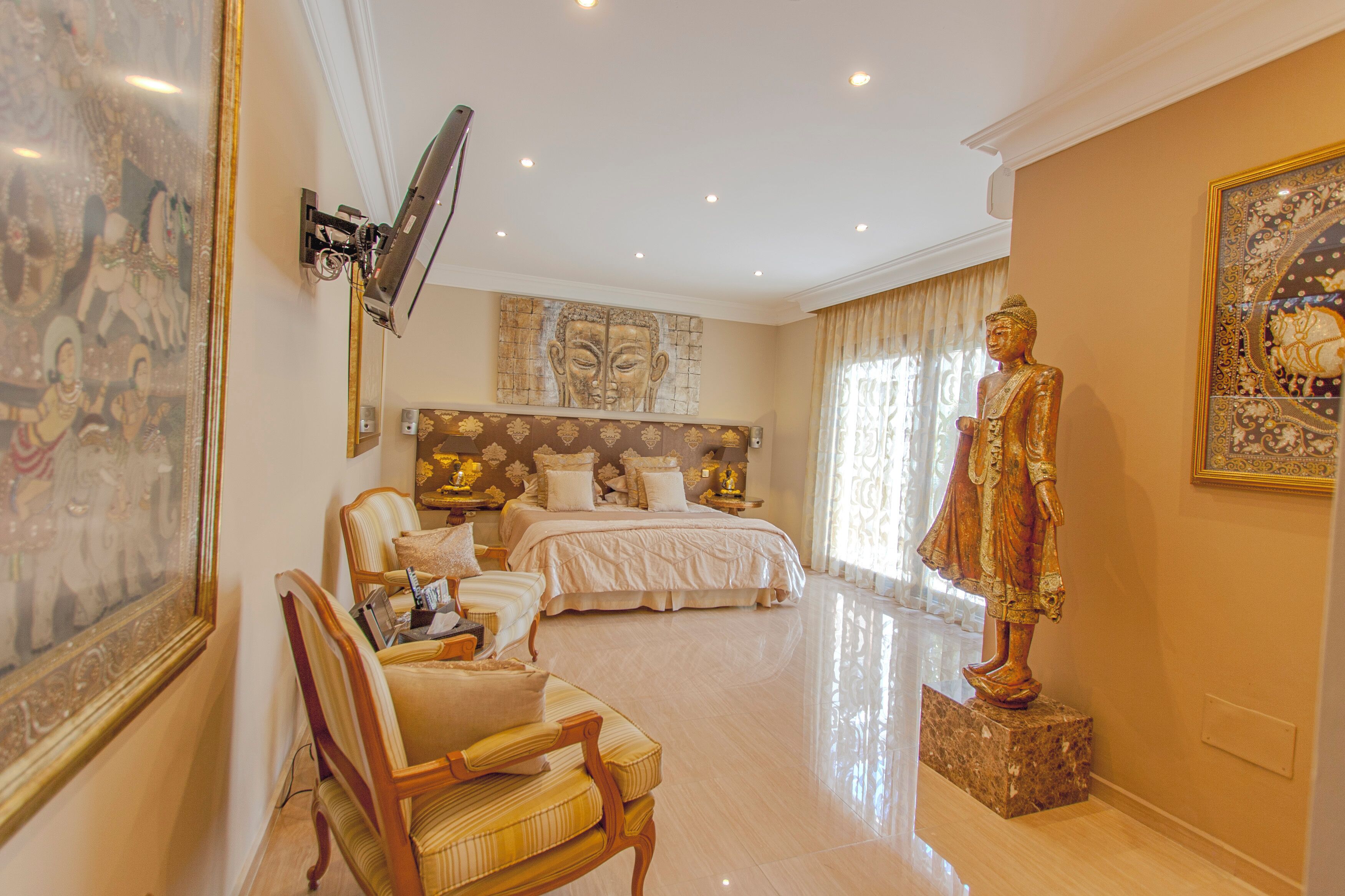 Un dormitorio amplio con una cama grande, una zona de estar con una silla, una estatua y obras de arte en las paredes.