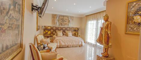 Un dormitorio amplio con una cama grande, una zona de estar con una silla, una estatua y obras de arte en las paredes.