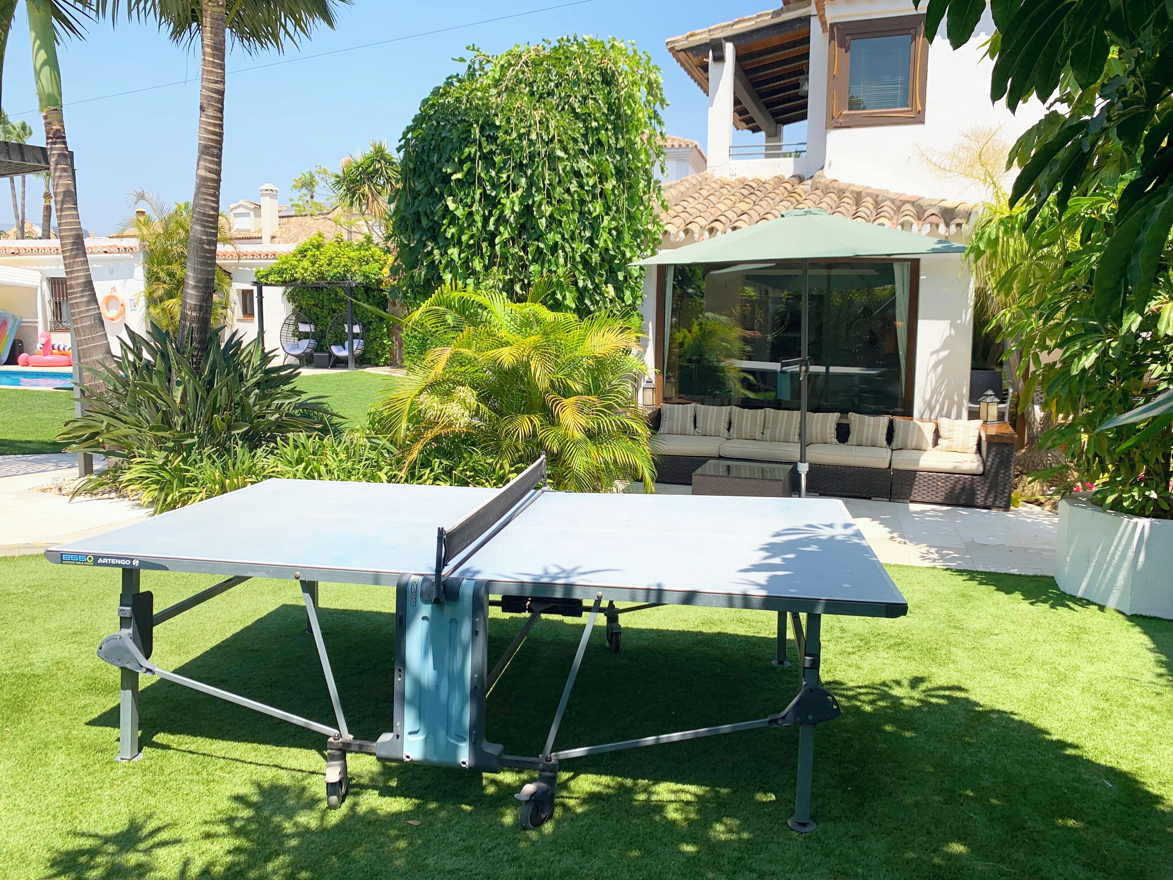 A ping pong table in a well-maintained garden with a pool and outdoor seating area.