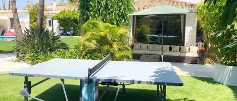 A ping pong table in a well-maintained garden with a pool and outdoor seating area.