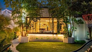 A well-lit outdoor area with a basketball hoop, surrounded by lush greenery and a pathway leading to a building with a visible interior. - Villa Turrión (Marbella)