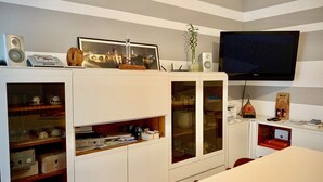 A modern living room with a flat-screen TV mounted on the wall, a dining table with chairs, and a kitchen area with cabinets and appliances. - Ariel B&B (Verona)