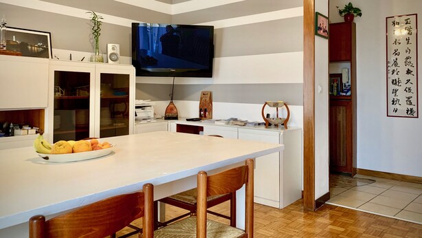 A modern kitchen with a flat-screen TV, wooden chairs, and a fruit bowl on the counter. - Ariel B&B (Verona)