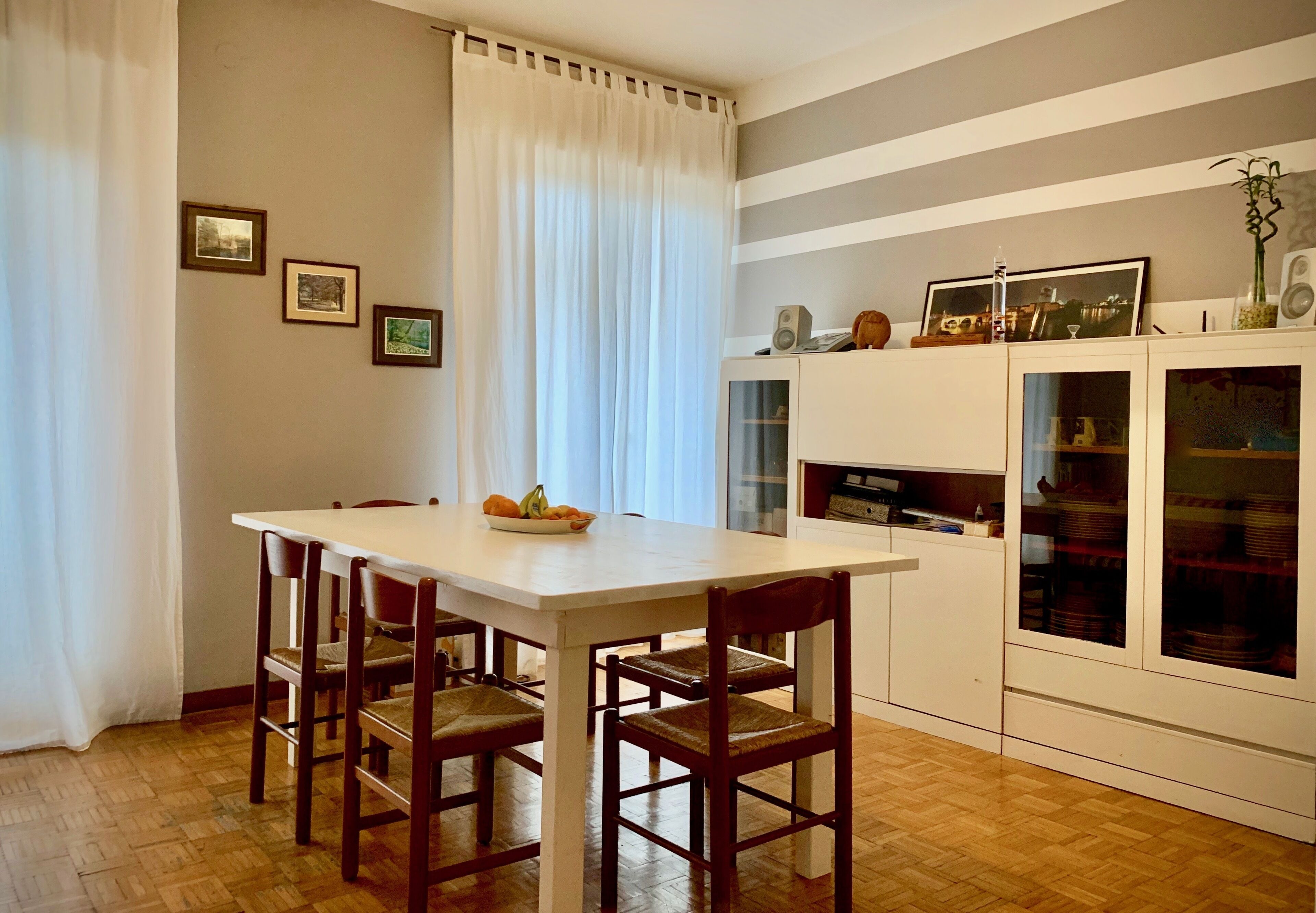 Un coin repas comprenant une table et des chaises, un meuble avec des portes en verre et une fenêtre avec des rideaux.