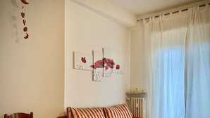 A living room with a red sofa, a wooden chair, and wall art depicting flowers. - Ariel B&B (Verona)