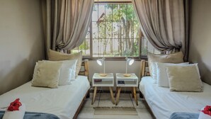 Habitación de hotel con dos camas, una ventana con cortinas, mesitas de noche con lámparas y vistas a zonas verdes.