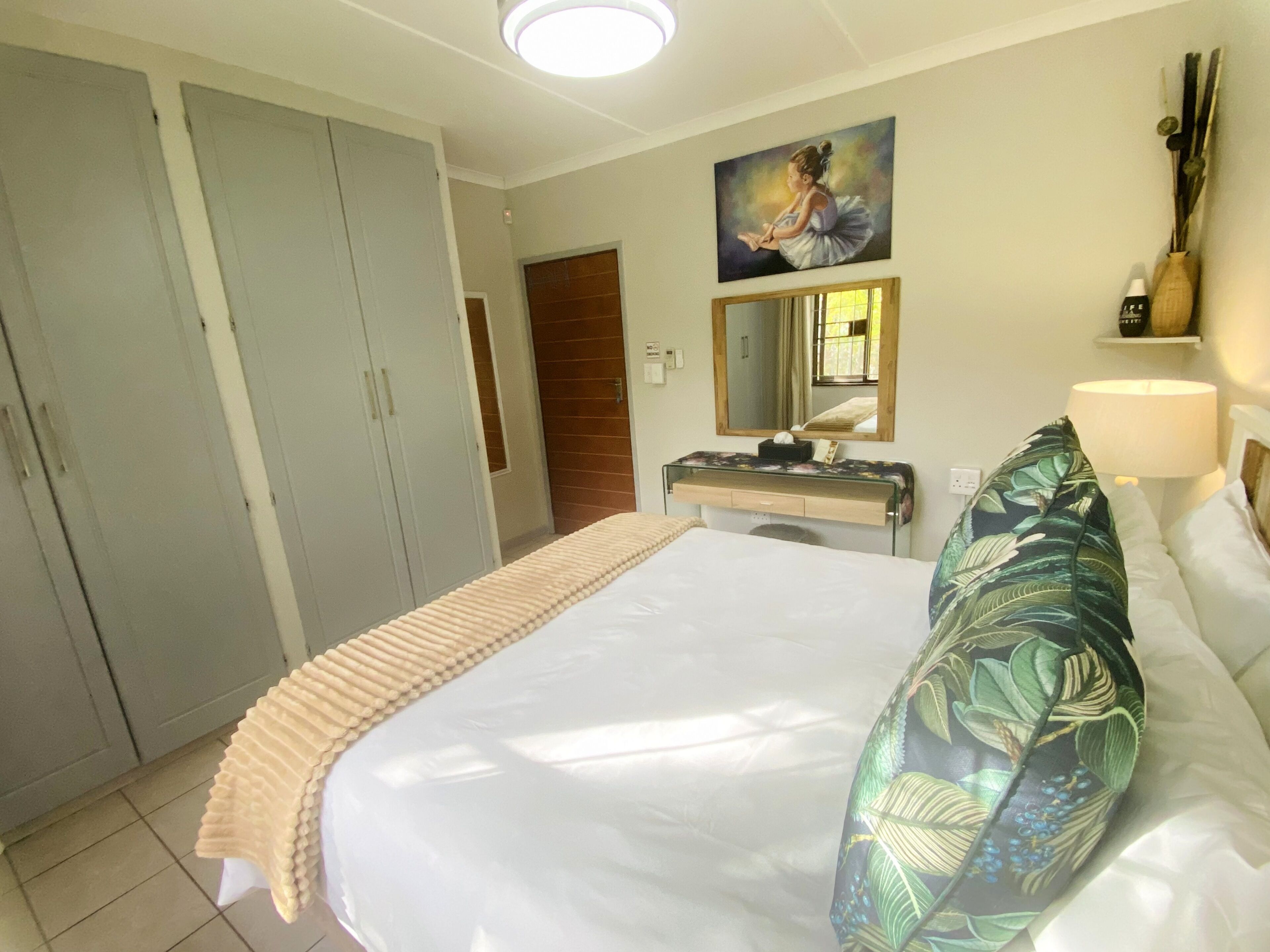 A hotel room with a bed, a desk, a wardrobe, a mirror, and a painting on the wall.