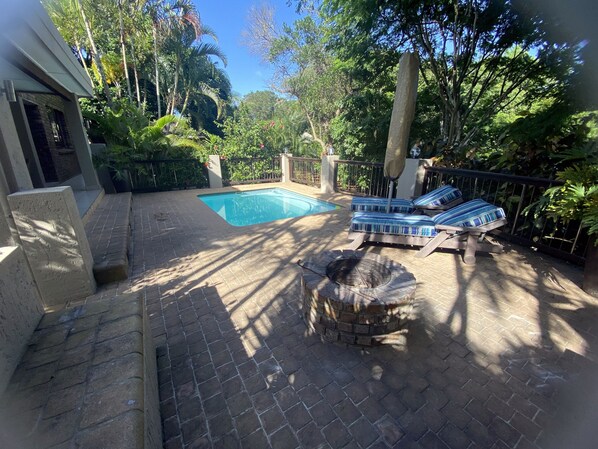 Un jardin avec une piscine, des chaises longues et un foyer extérieur.