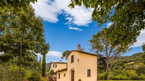 Un petit bâtiment jaune, surmonté d’un toit en tuiles, entouré d’une végétation luxuriante et d’arbres.