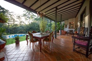 A covered patio with a dining table and chairs, surrounded by potted plants and a view of a swimming pool. - Karen Gables (Nairobi)