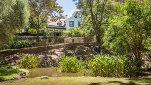 Un jardín con un estanque, un puente de piedra y una casa al fondo.