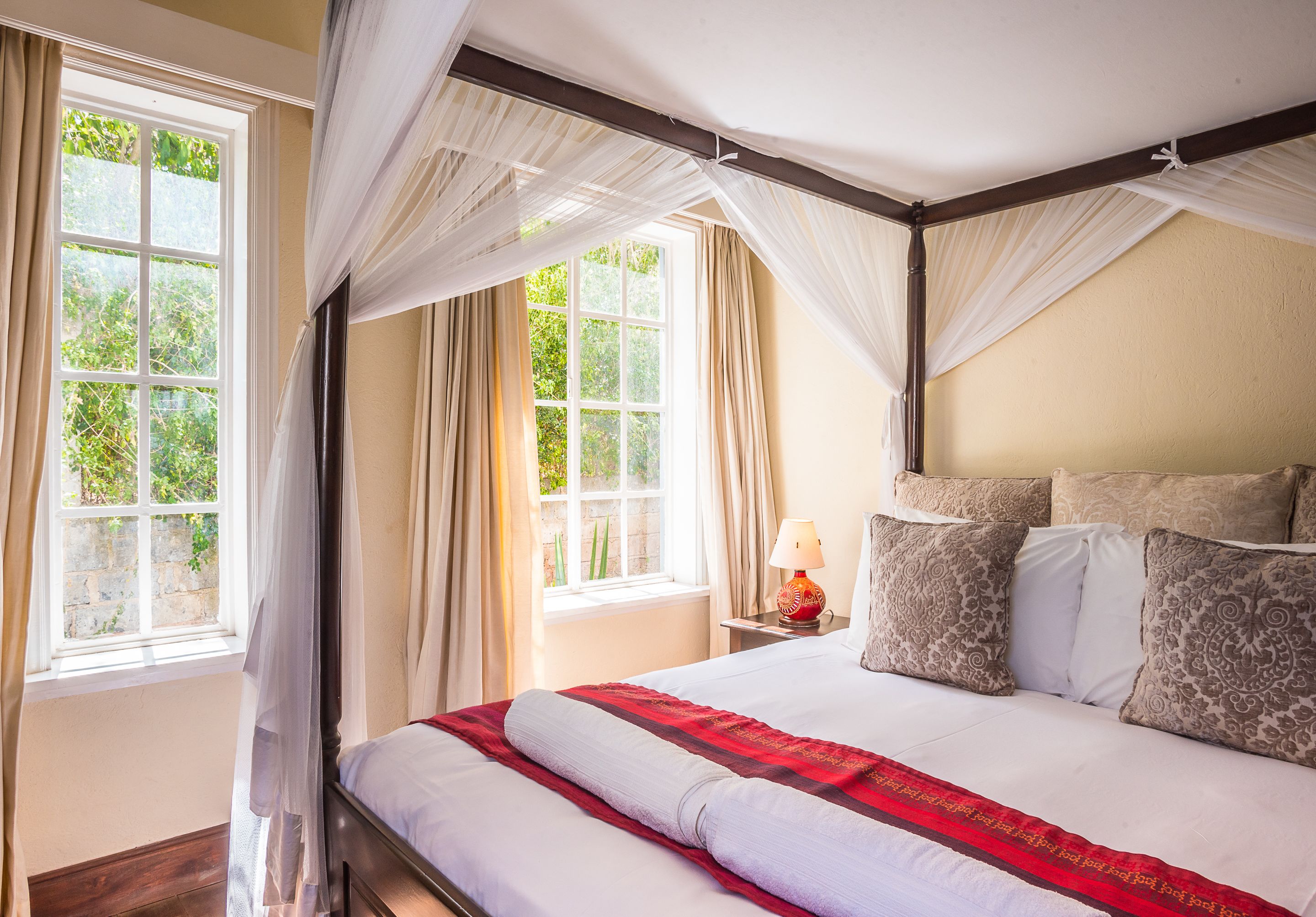 A bedroom with a large bed, a nightstand, a lamp, and a window with curtains.