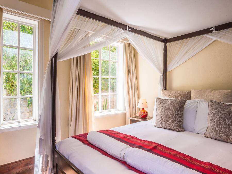 A bedroom with a large bed, a nightstand, a lamp, and a window with curtains.