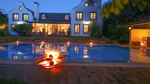 Una casa grande con piscina, un pozo de fuego y un jardín bien cuidado.