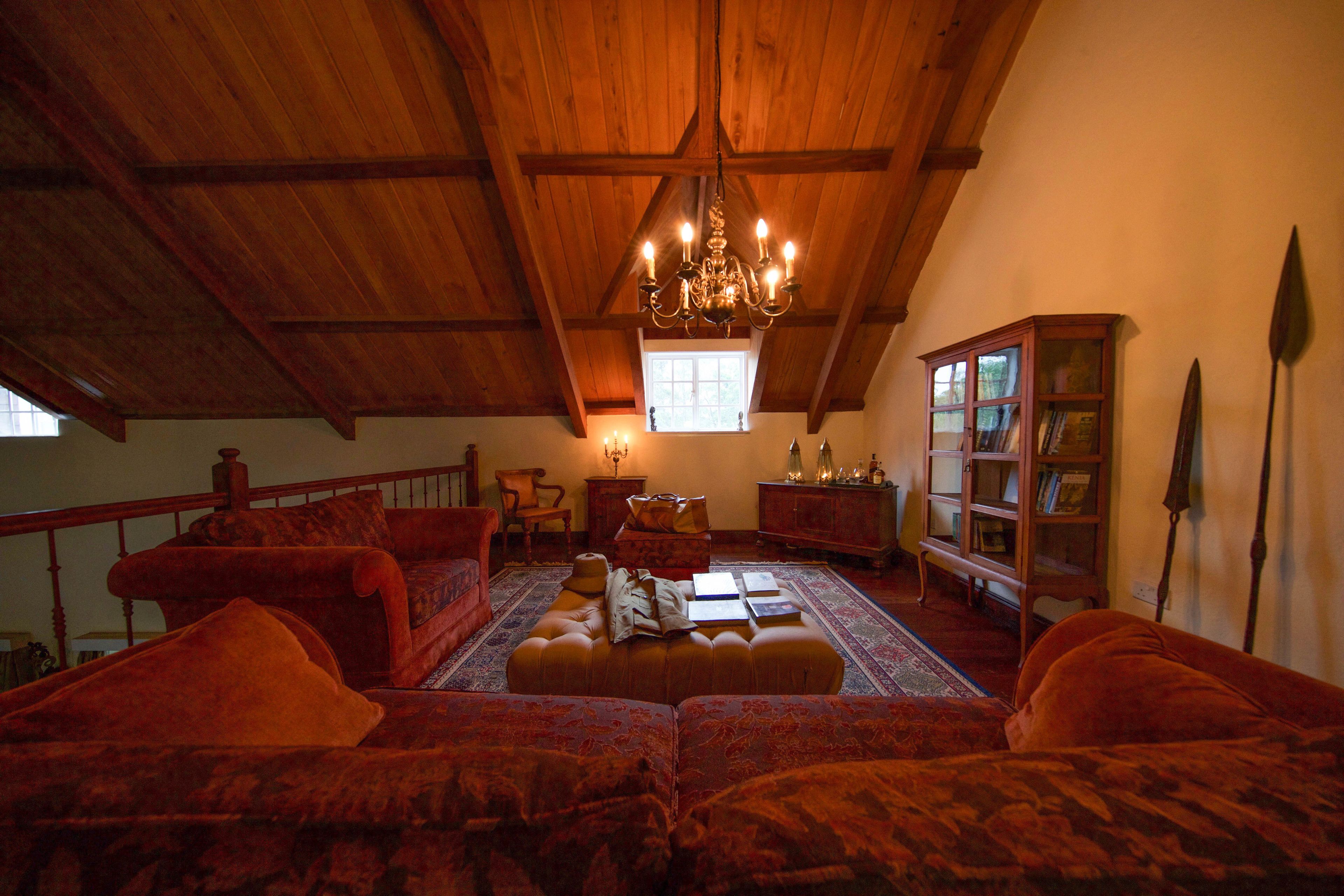 Une pièce chaleureuse de style loft, avec un plafond haut, des poutres en bois, un lustre, une grande fenêtre, une cheminée, ainsi qu’une collection de livres et d’objets décoratifs.