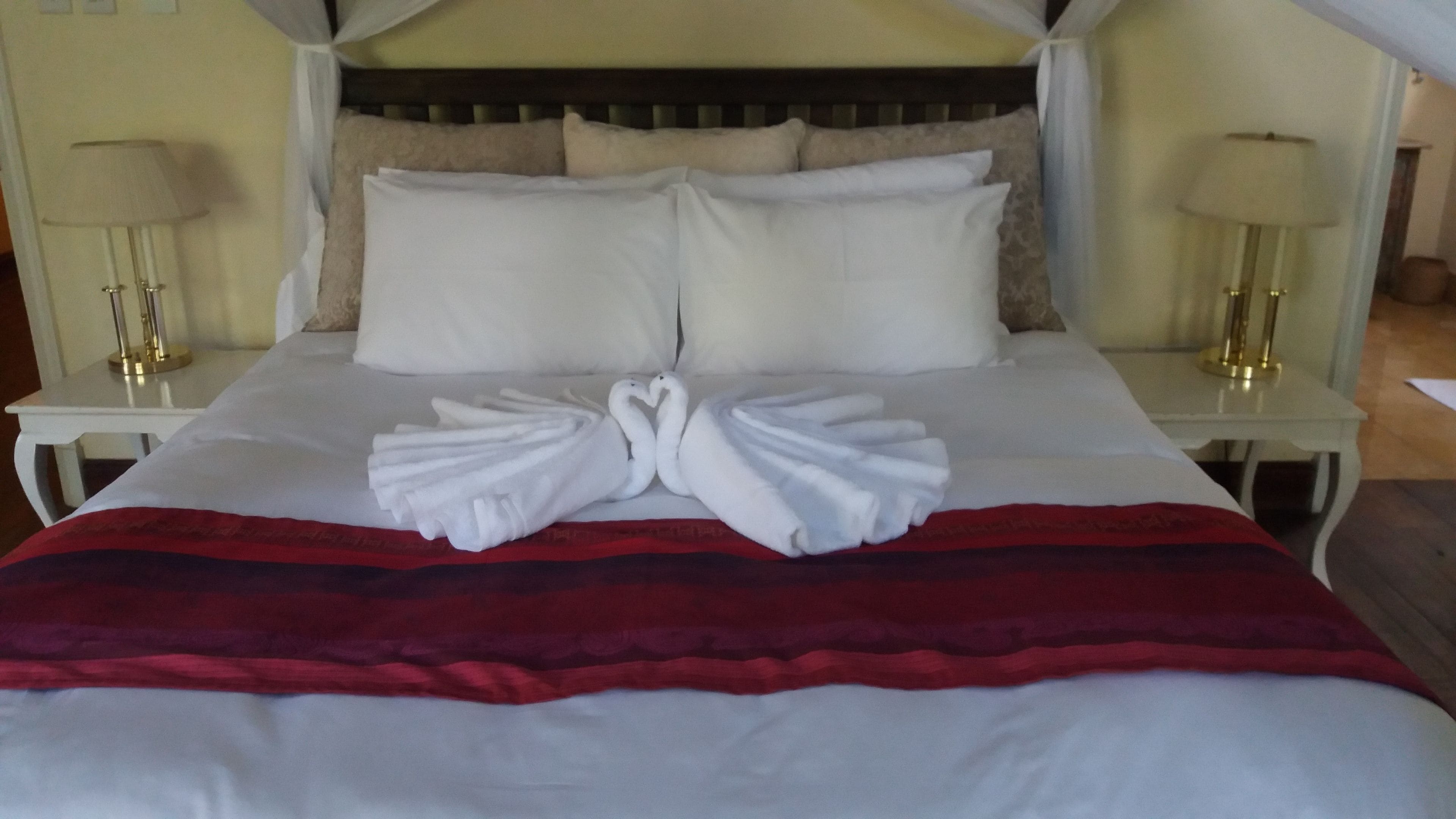 Ein Hotelzimmer mit einem großen Bett, weißen Laken, einer rot-schwarz gestreiften Decke und zwei Nachttischen mit Lampen.