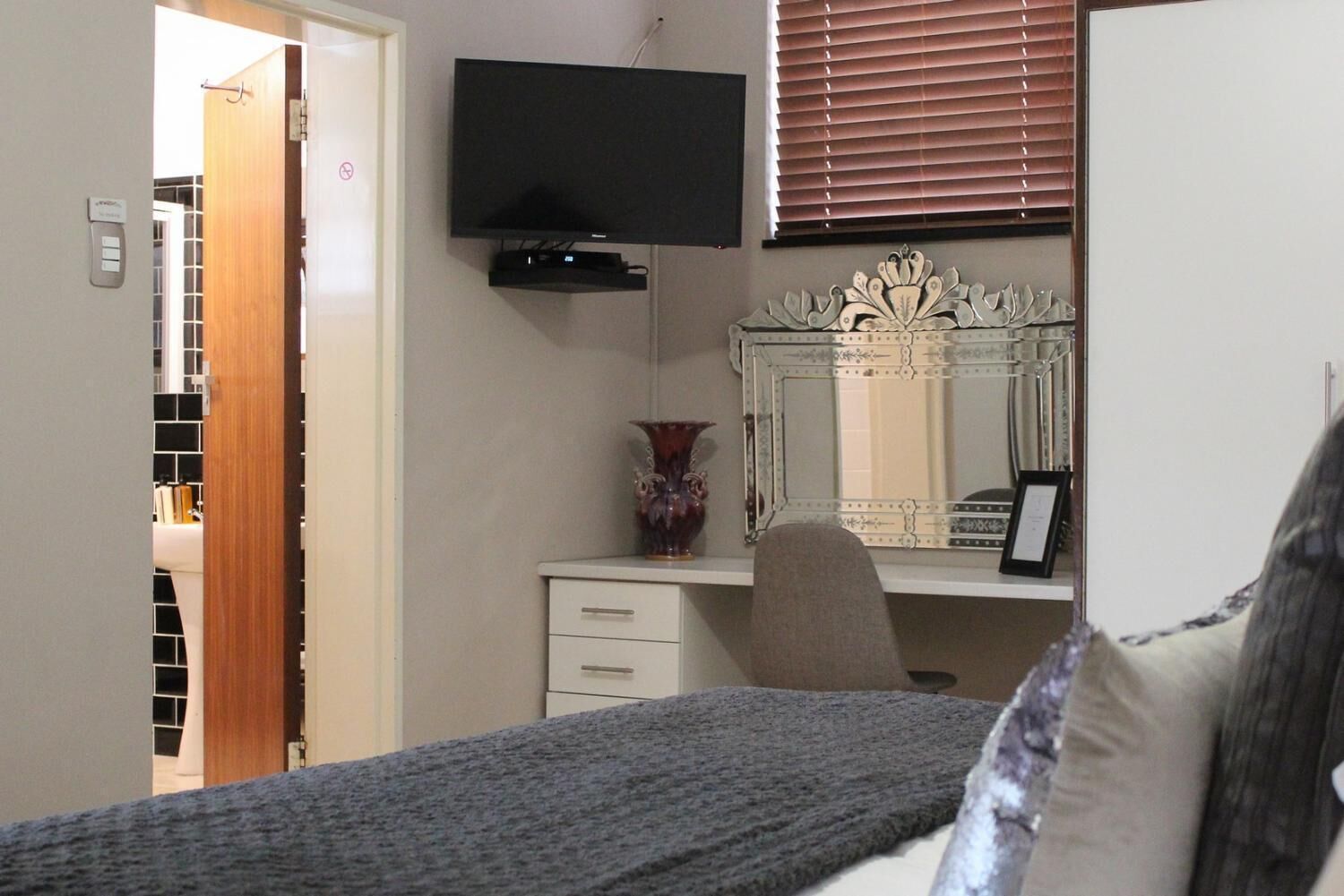 Un dormitorio con cama, cómoda, televisor montado en la pared y espejo con marco decorativo.