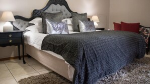 A bedroom with a tufted headboard, a large bed with a dark blanket, two bedside tables with lamps, and a red chair. - A Queenslin Guesthouse (Paarl)