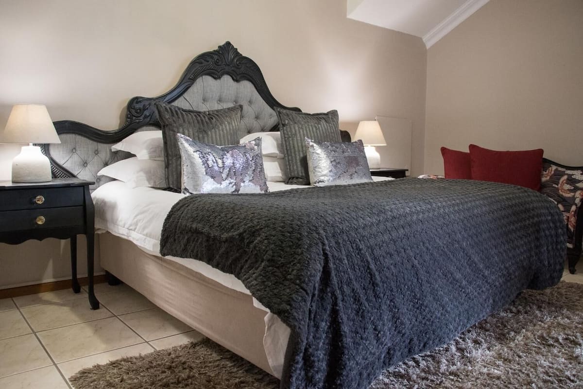 A bedroom with a tufted headboard, a large bed with a dark blanket, two bedside tables with lamps, and a red chair.