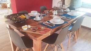 A wooden dining table set with plates, bowls, and cutlery, surrounded by chairs. - A Queenslin Guesthouse (Paarl)
