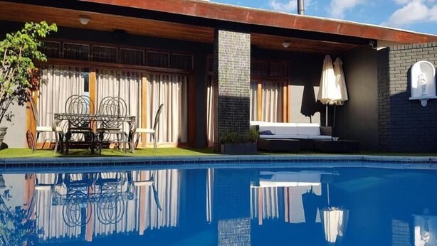 A modern pool area with a clear blue pool, a wooden deck, and a seating area with a sofa and chairs. - A Queenslin Guesthouse (Paarl)