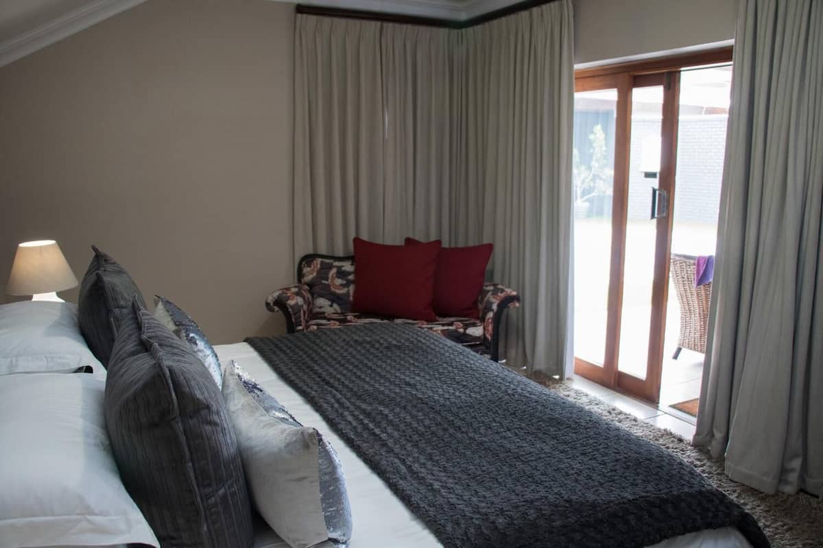 A hotel room with a large bed, a chair with red cushions, and a view of the outdoors through a glass door.