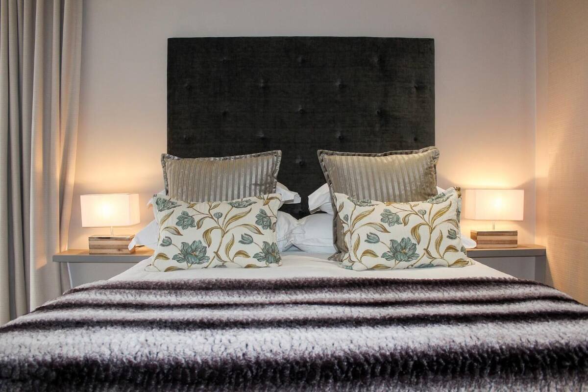 A neatly made bed with striped bedding, two bedside lamps, and floral-patterned pillows.