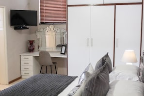 A bedroom with a bed, a desk with a chair, a television, a wardrobe, and a bedside lamp. - A Queenslin Guesthouse (Paarl)