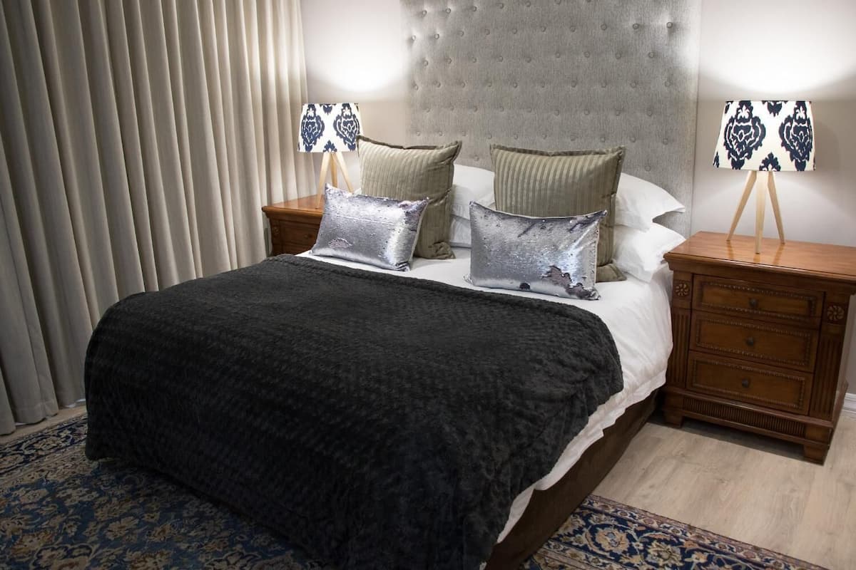 A hotel room with a large bed, two bedside tables with lamps, a headboard, and a patterned rug.