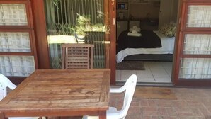 A room with a wooden table and chairs, a bed with a black and white bedspread, and a window with metal bars. - A Queenslin Guesthouse (Paarl)