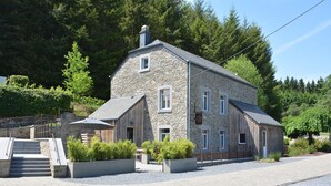 A stone building with a sloped roof, a wooden door, and a staircase leading to a covered area with plants. - Holiday Home in Gedinne by the River (Vencimont)
