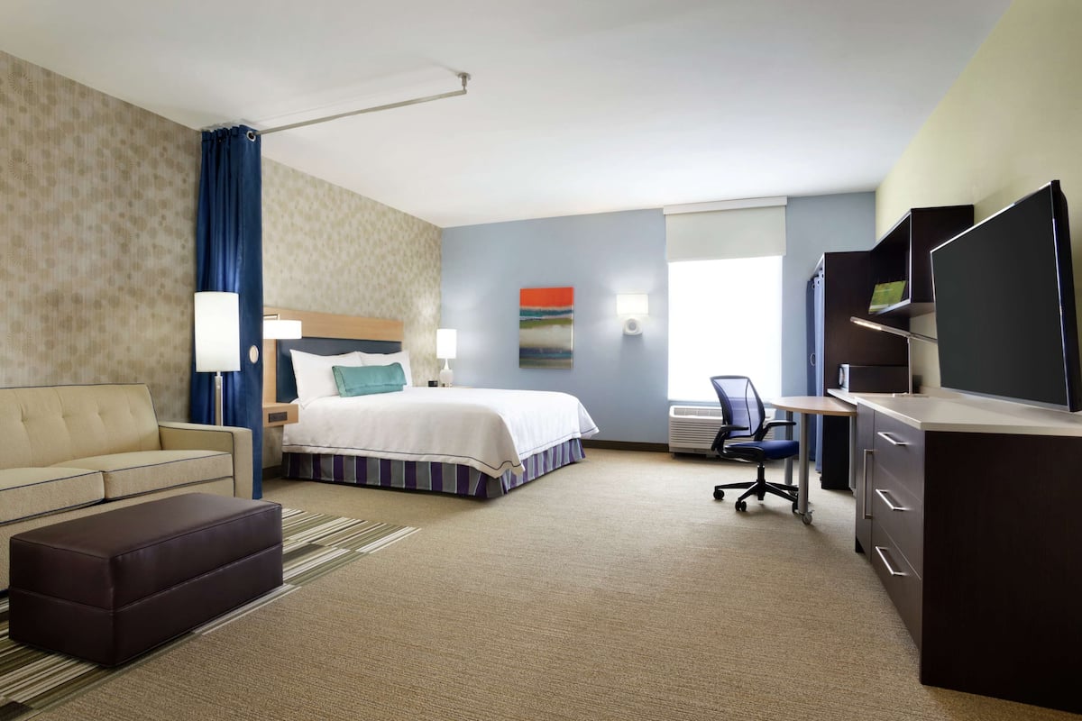 A hotel room with a bed, a sofa, a desk, a TV, and a window.