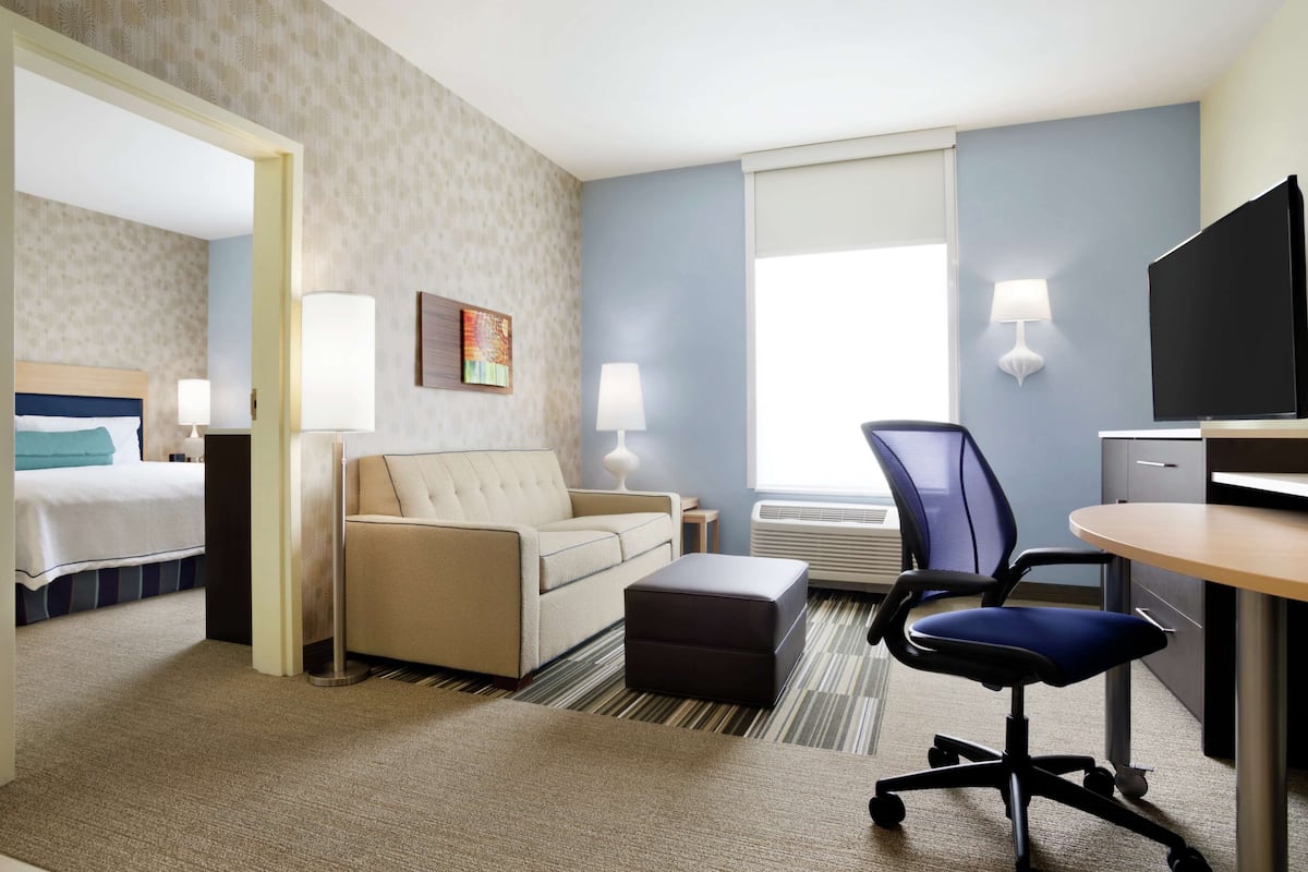 A hotel room with a bed, a sofa, a desk, a chair, and a TV.