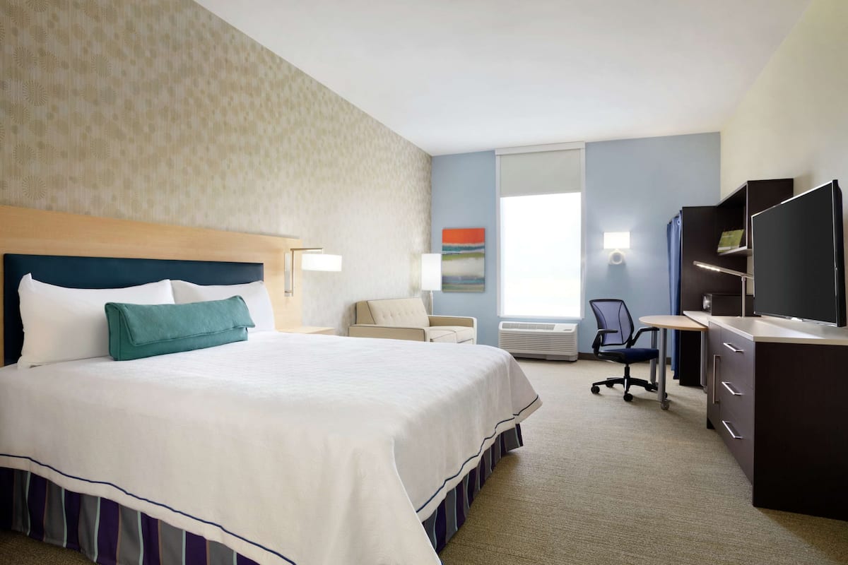 A hotel room with a large bed, a desk, a chair, and a television.
