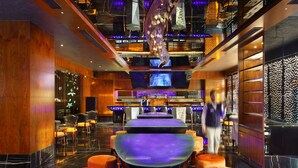 A modern bar area with a long counter, multiple seating options, and a large screen displaying content. - Radisson Blu Jammu (Jammu)