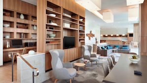 A modern living room with built-in wooden shelving, a flat-screen TV, comfortable seating, and a dining area. - Element by Marriott Dallas Love Field (Dallas)