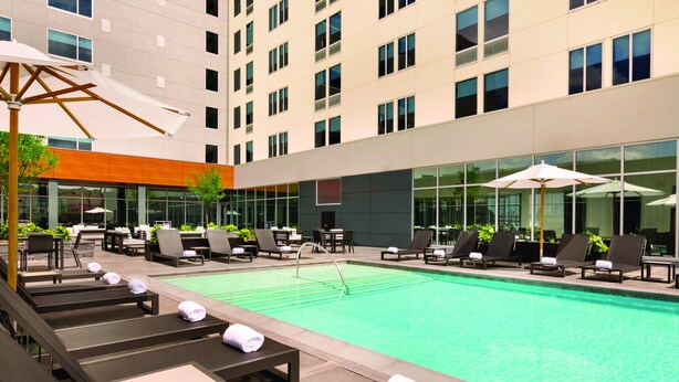 A hotel pool area with sun loungers, umbrellas, and a modern building facade. - Element by Marriott Dallas Love Field (Dallas)