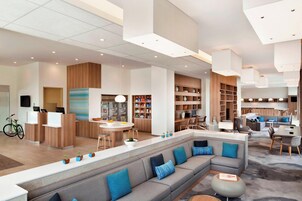 En moderne hotellobby med reception, siddeområde, køkken og spiseplads.