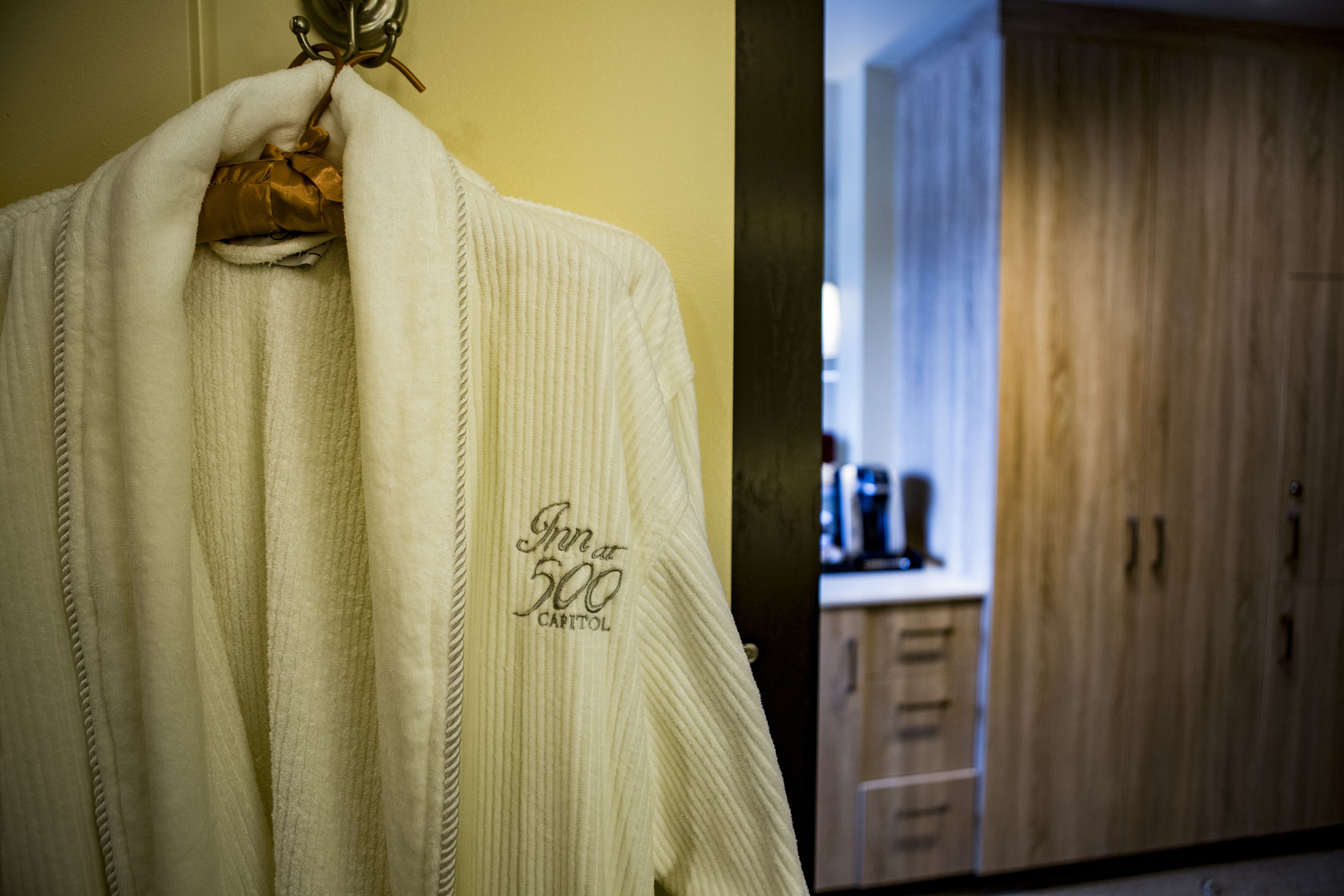 A hotel robe with a logo and a glimpse of a wooden wardrobe and kitchen area in the background.