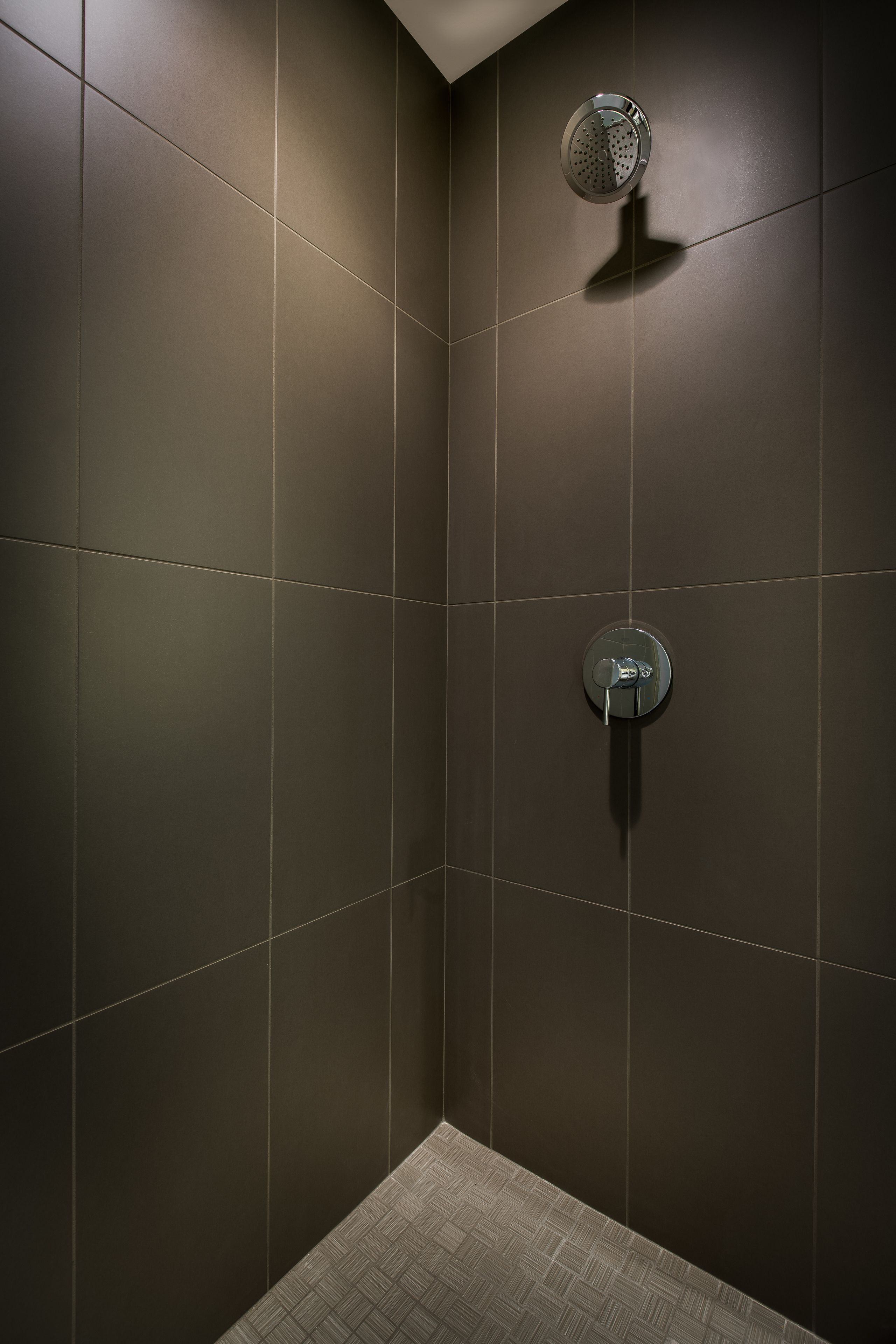 A modern shower area with dark tiles and a visible showerhead.