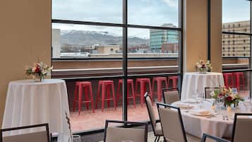 Comedor con mesas dispuestas para una comida, ventanas amplias con vista a montañas y un candelabro.