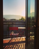 A balcony with a red folding chair and a table, overlooking a cityscape with mountains in the distance.