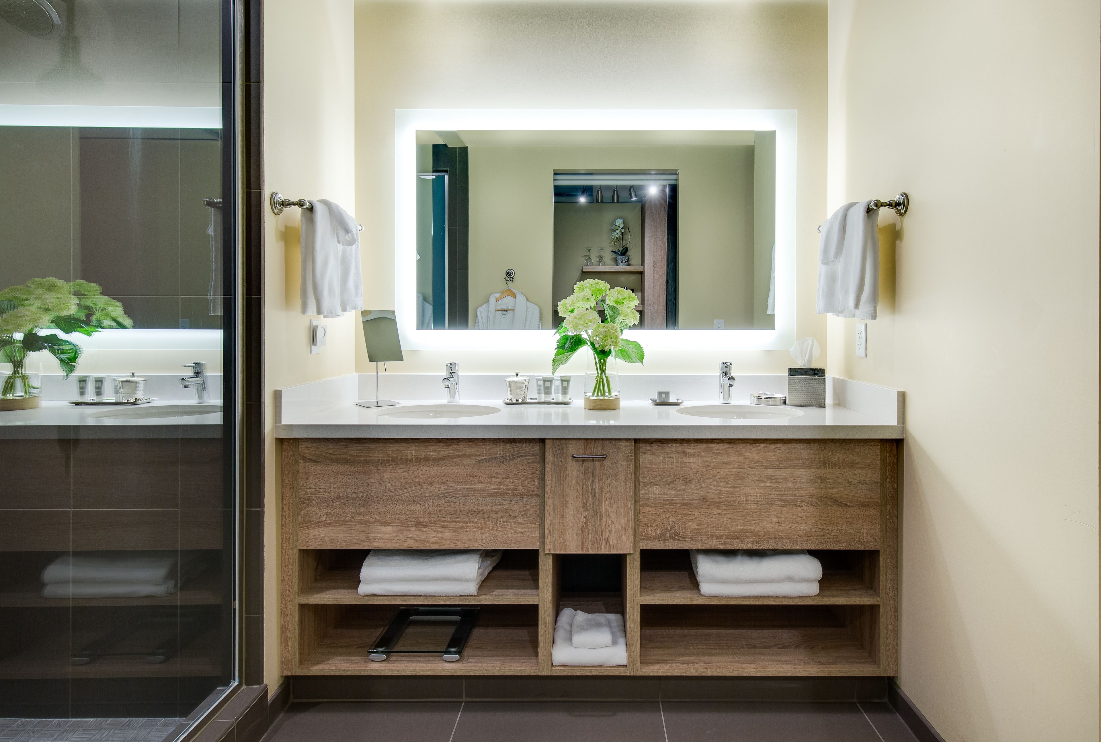 A modern bathroom with a double sink vanity, wooden cabinets, and a large mirror.