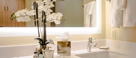A bathroom with a white sink, a mirror, and a vase with white flowers.