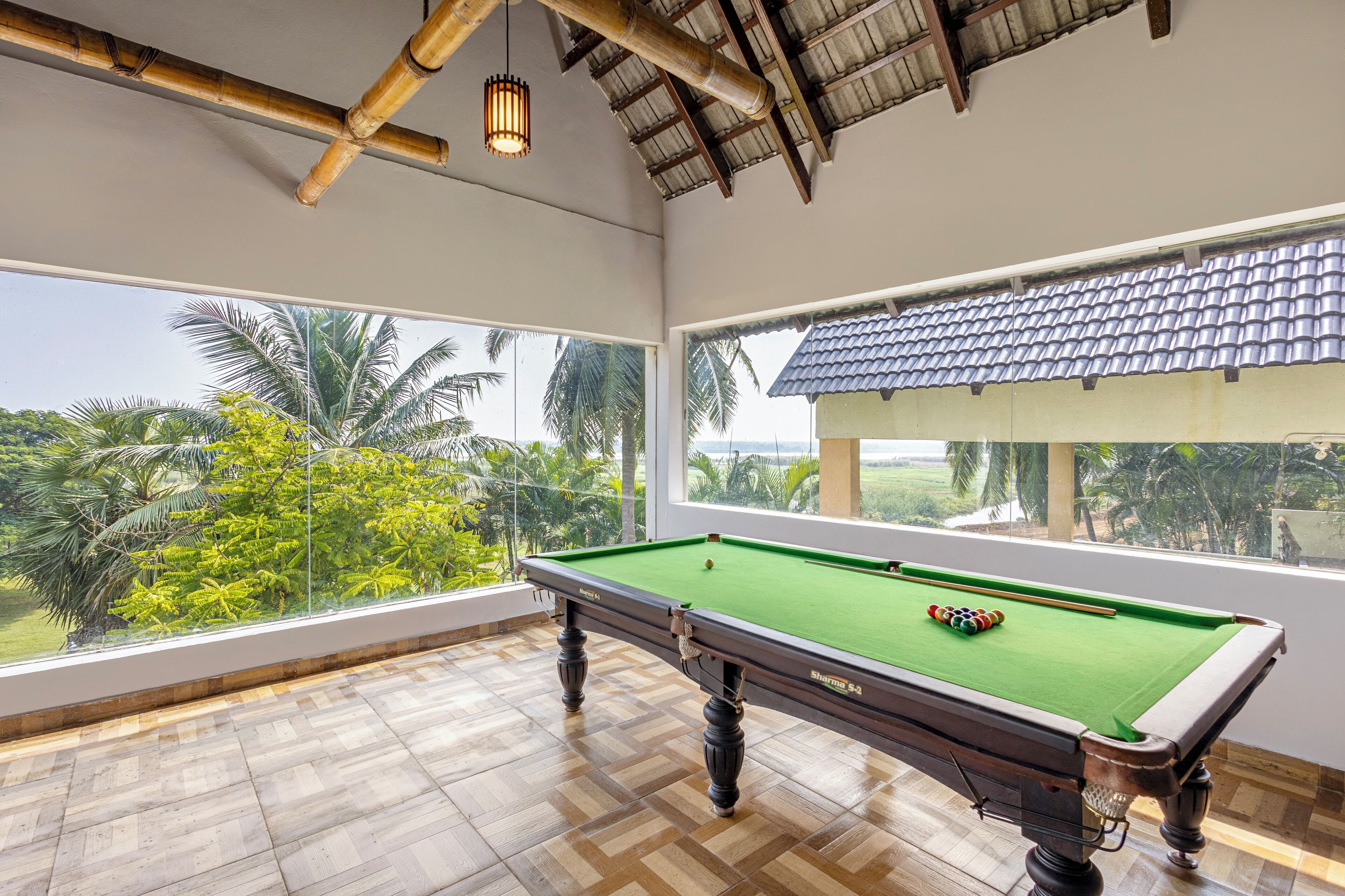 A pool table in a room with large windows overlooking a tropical landscape.