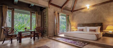 Una habitación amplia con una cama grande, una mesa de comedor con sillas y vistas a zonas verdes a través de las ventanas.