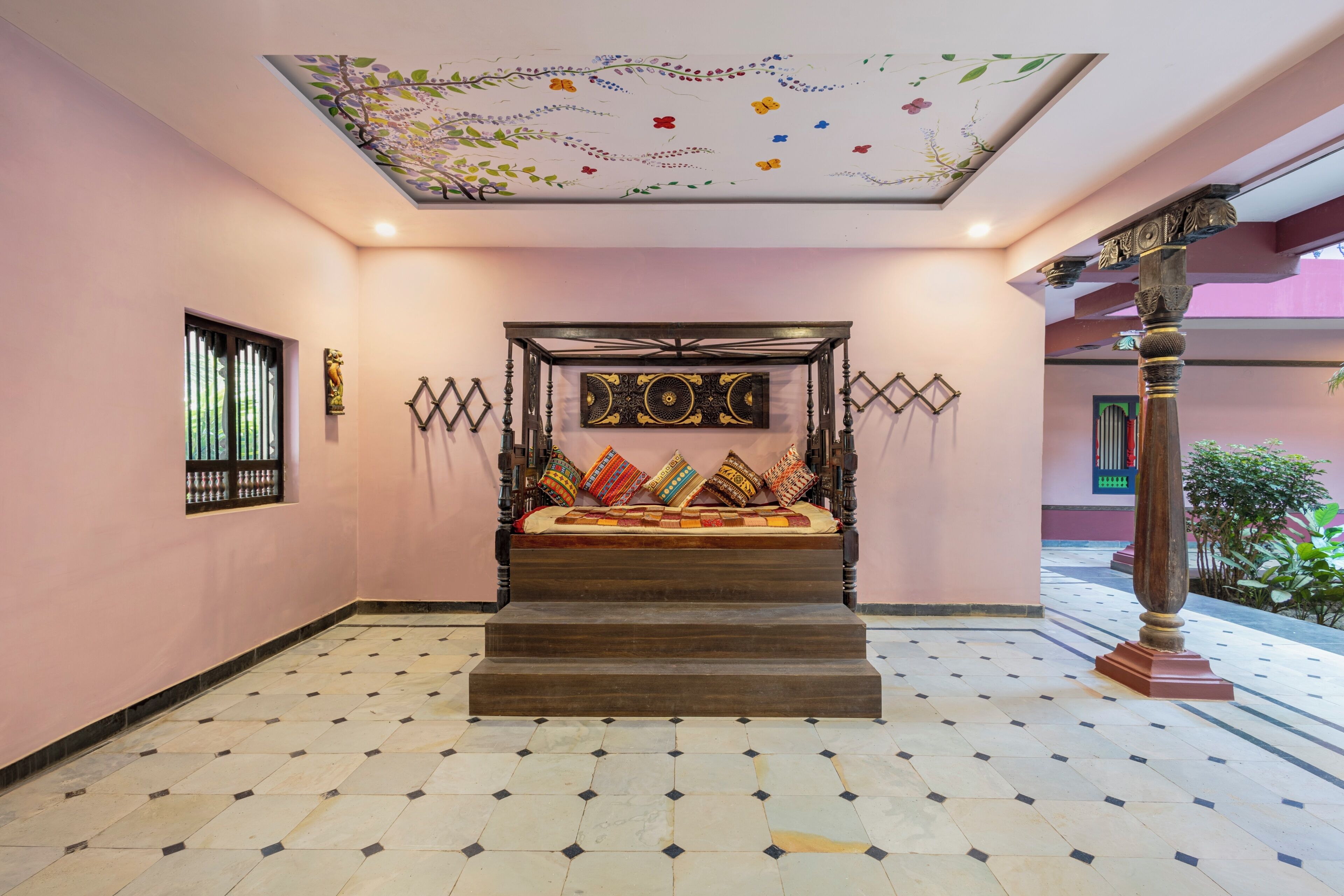 Escadaria que leva a uma cama com colcha estampada, teto com detalhes artísticos florais e janela com grades.