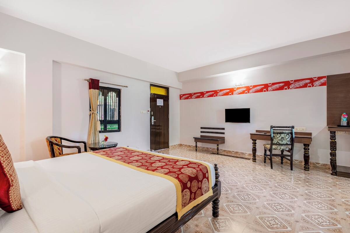 A hotel room with a large bed, a desk, a chair, a television, and a patterned floor.