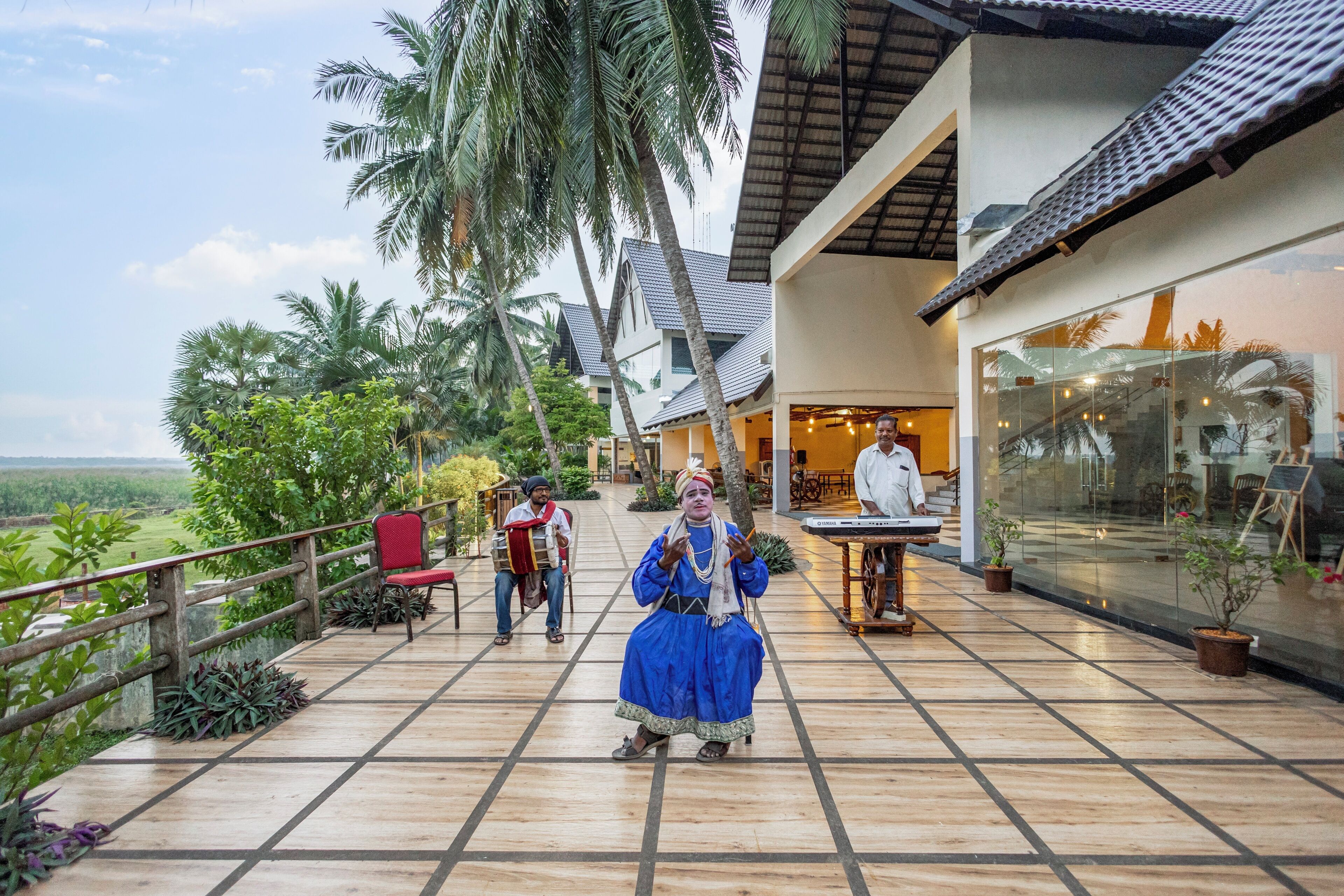 A terrace with a view of the landscape, palm trees, and a building with a tiled roof.