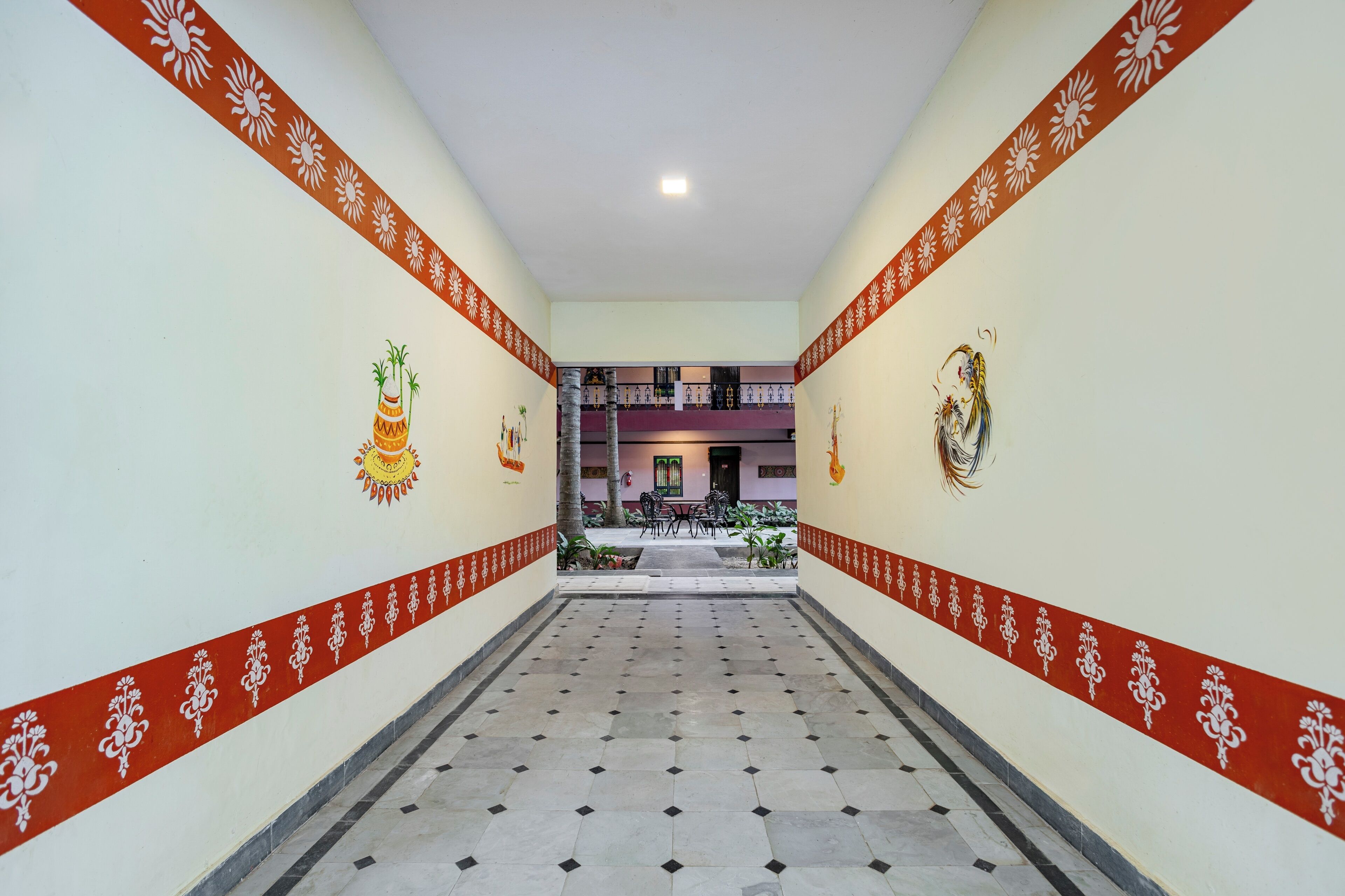 Un couloir aux murs décorés de motifs et au sol carrelé, qui mène à un espace détente avec des tables et des chaises.